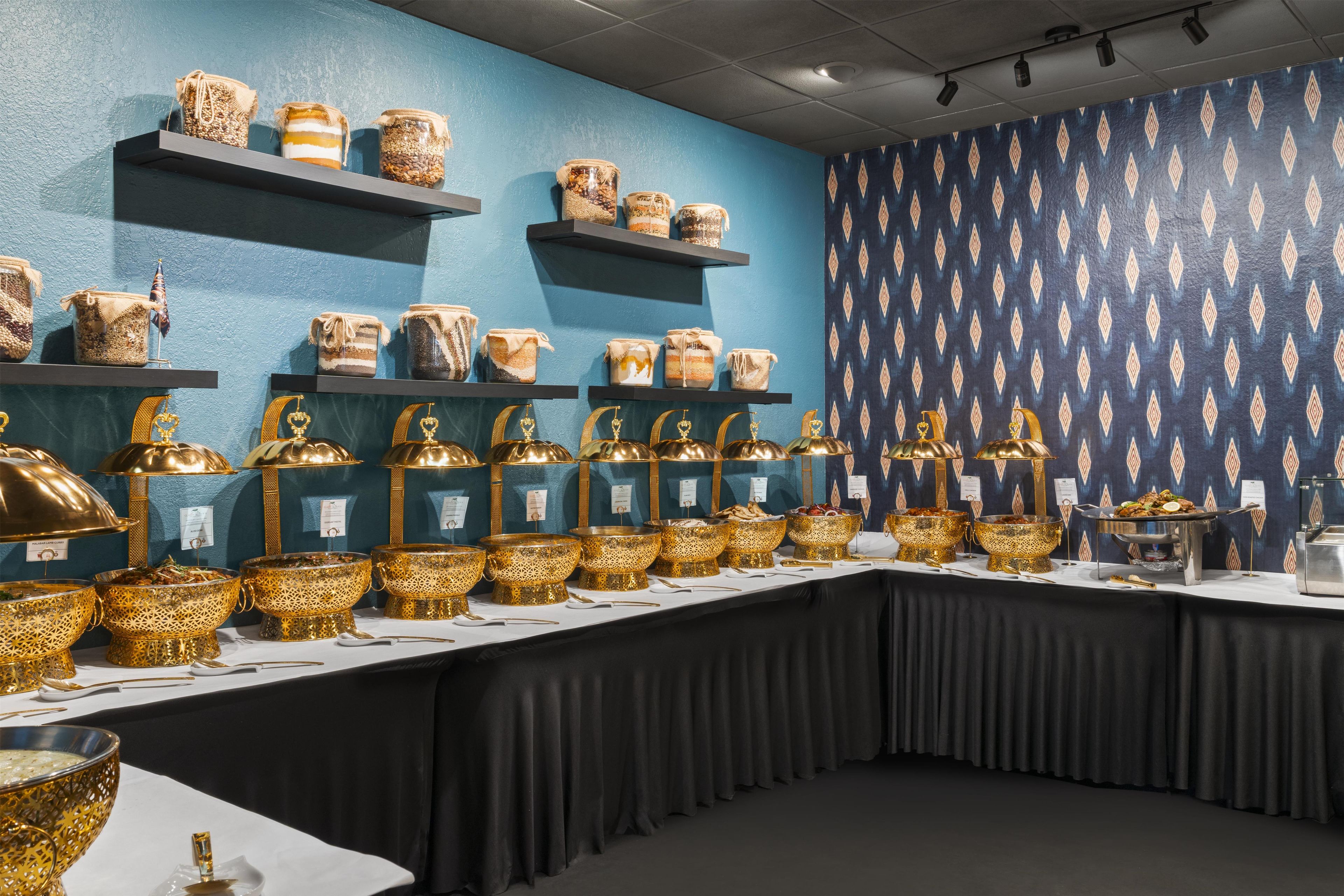 Mesa de buffet com diversos alimentos e douradas tigelas decorativas.