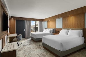 A hotel room with two beds, a desk, a chair, and a TV.