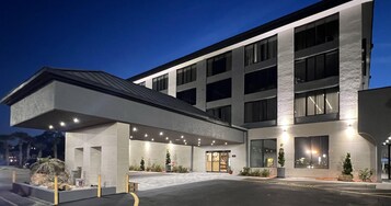 Un hotel moderno con entrada cubierta, ventanas amplias y zona de estacionamiento.