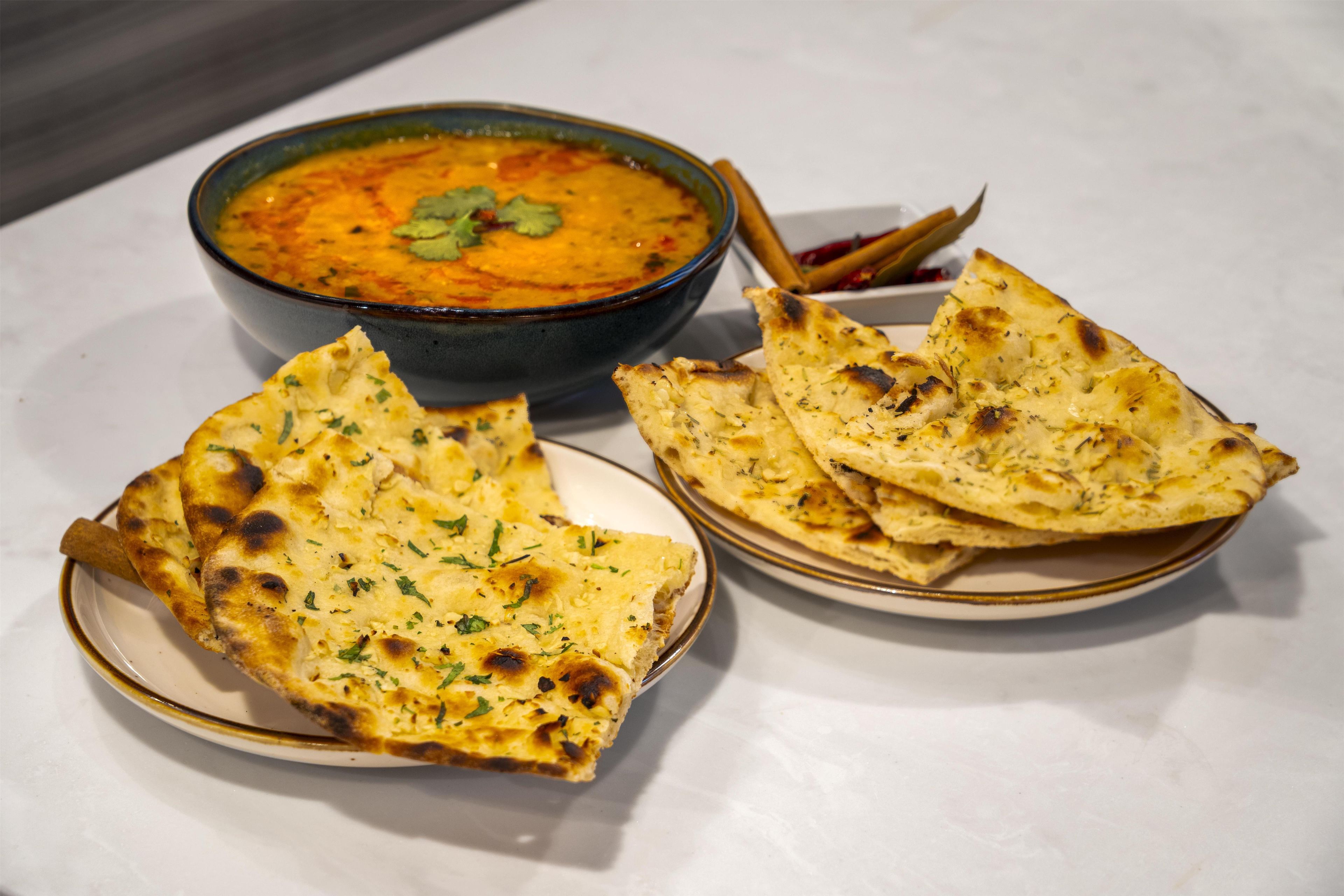 A bowl of soup with a garnish on a plate, accompanied by pieces of flatbread.