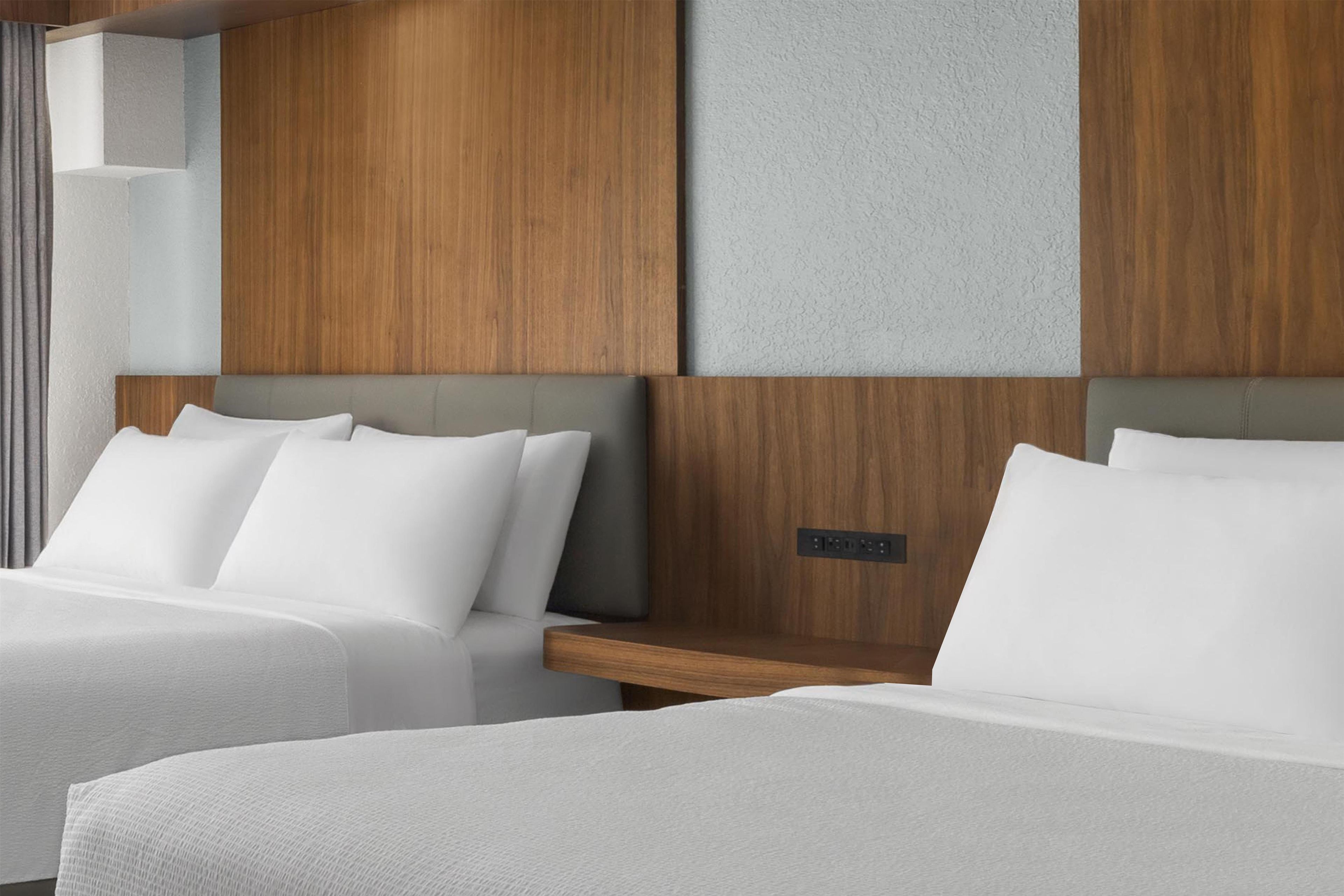 A hotel room with two beds, a wooden headboard, and a control panel.