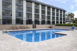 A modern hotel with a rectangular swimming pool, lounge chairs, and a landscaped area with potted plants.