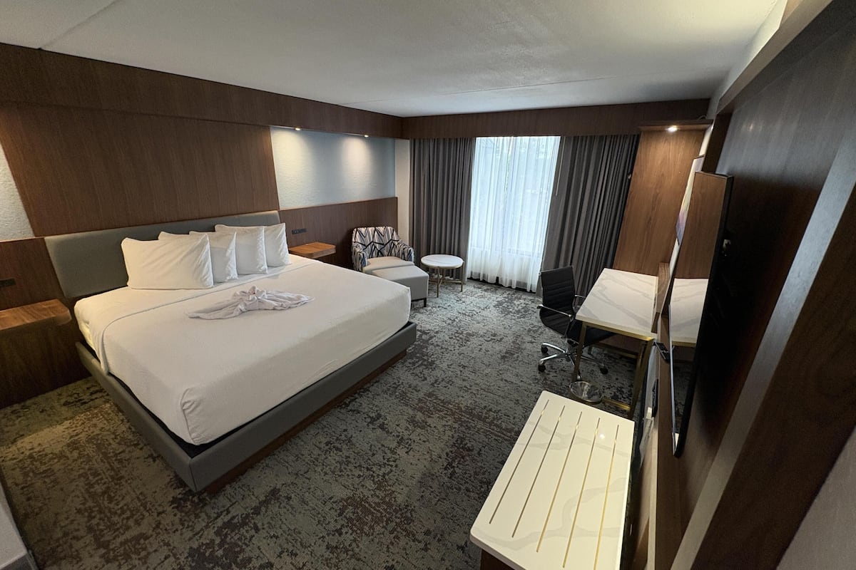 A hotel room with a large bed, a desk, a chair, a small table, and a mirror.