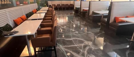 Un restaurante con cabinas y mesas, piso de mármol e iluminación colgante.