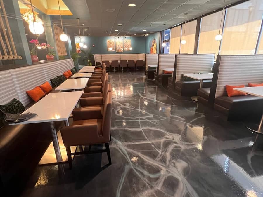 Un restaurante con cabinas y mesas, piso de mármol e iluminación colgante.