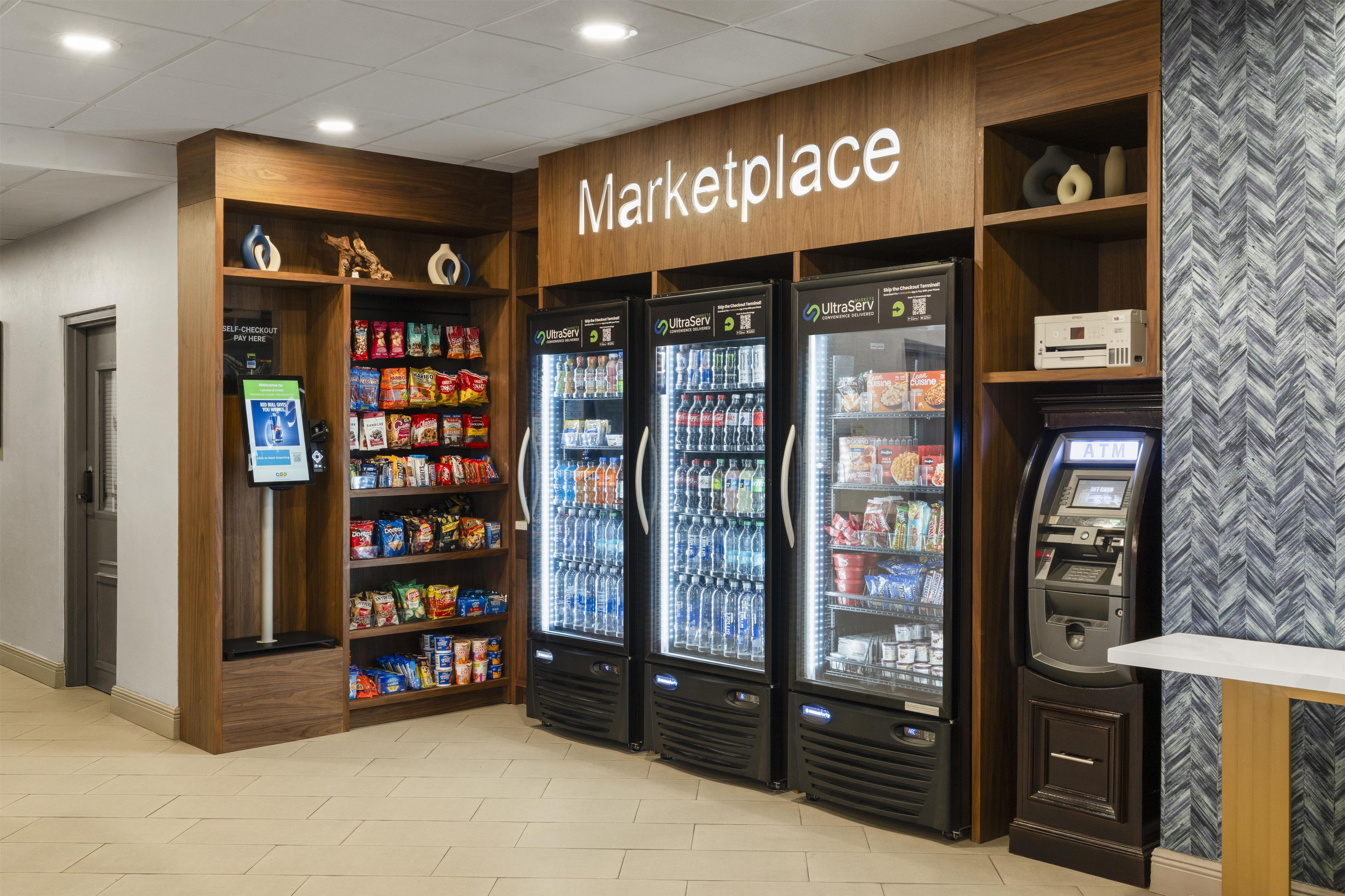 A self-checkout area with a sign reading 'Marketplace' above vending machines and snack shelves.