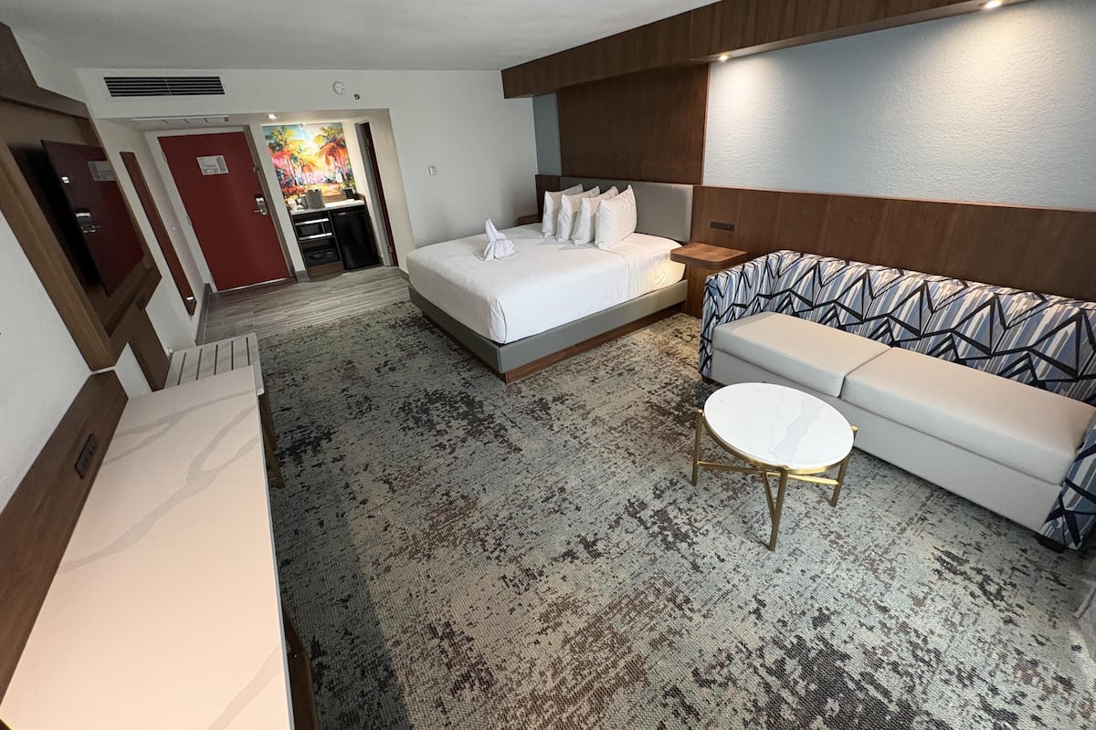 A hotel room with a bed, a sofa, a small round table, a door, and a wall with a wooden panel.