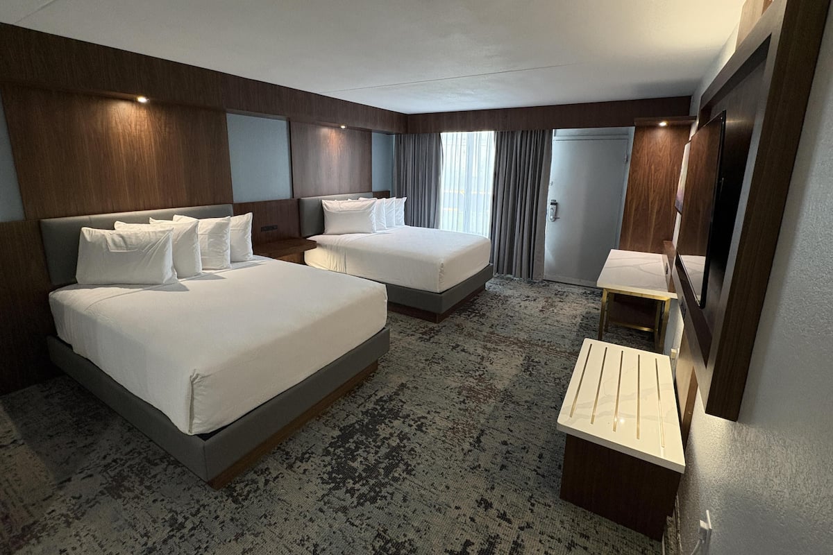 A hotel room with two beds, a small desk, a mirror, and a wardrobe.