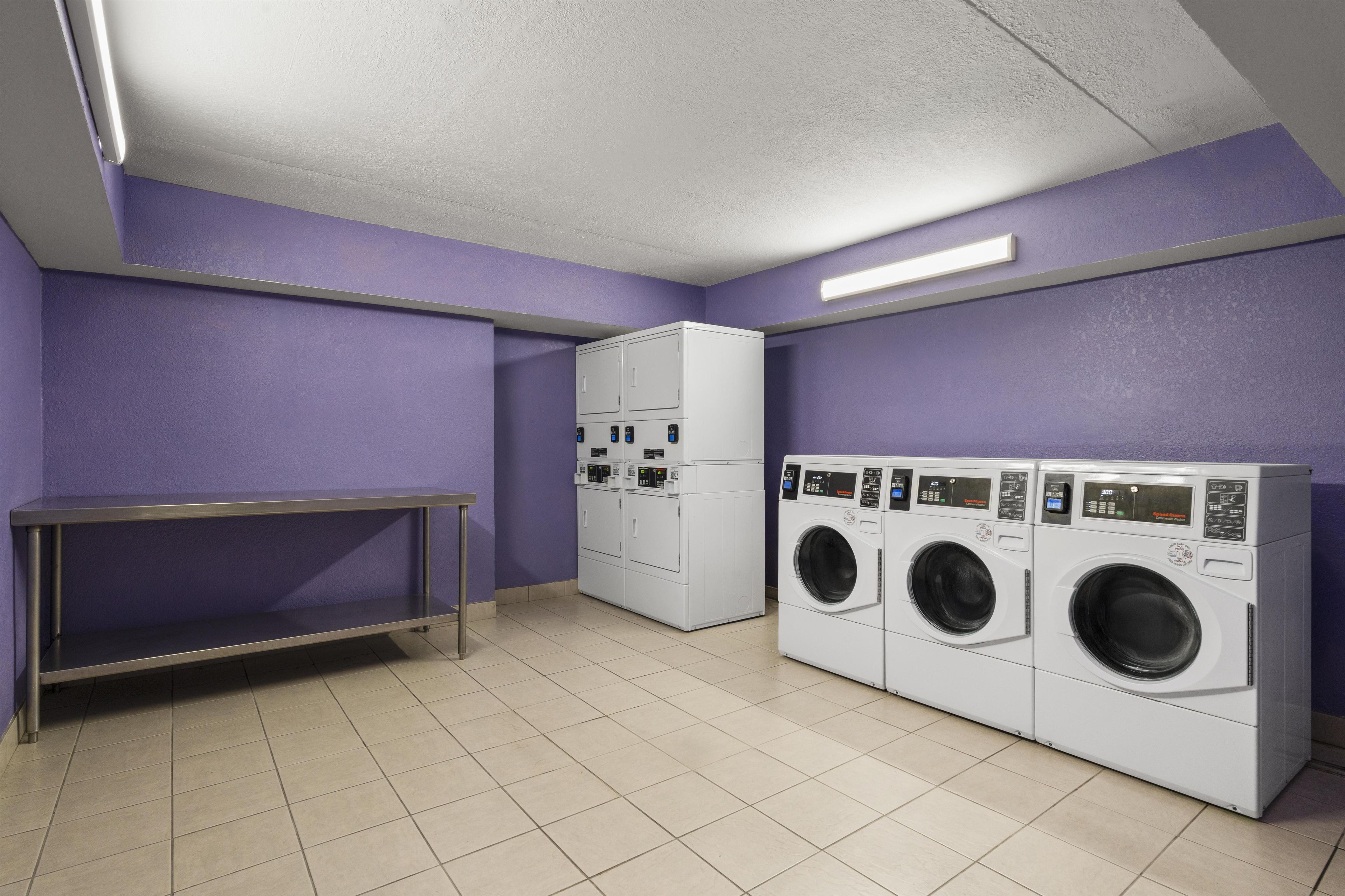 A laundry room with three stacked washing machines, a metal bench, and a tiled floor.