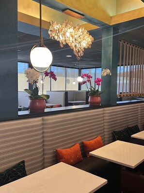 A restaurant interior with a modern design, featuring striped seating, hanging pendant lights, and potted orchids.
