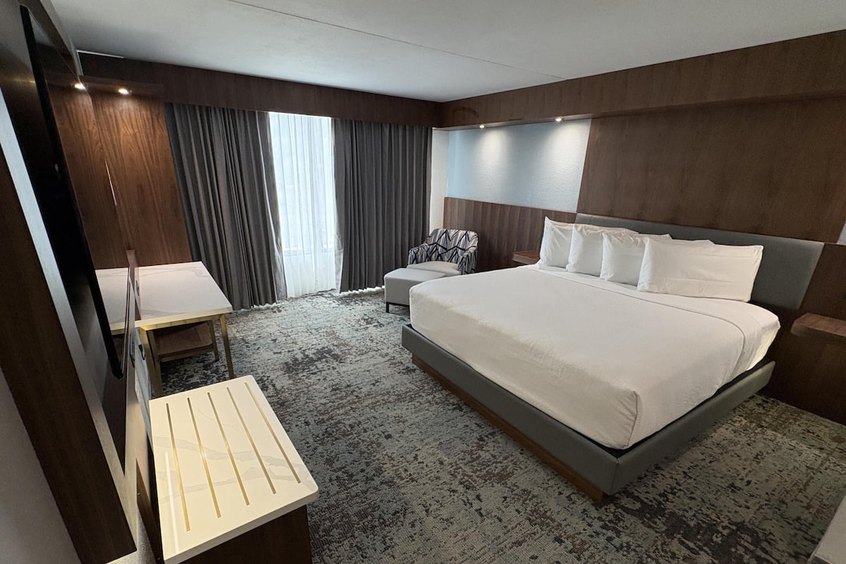 A modern hotel room with a large bed, a desk, and a chair.