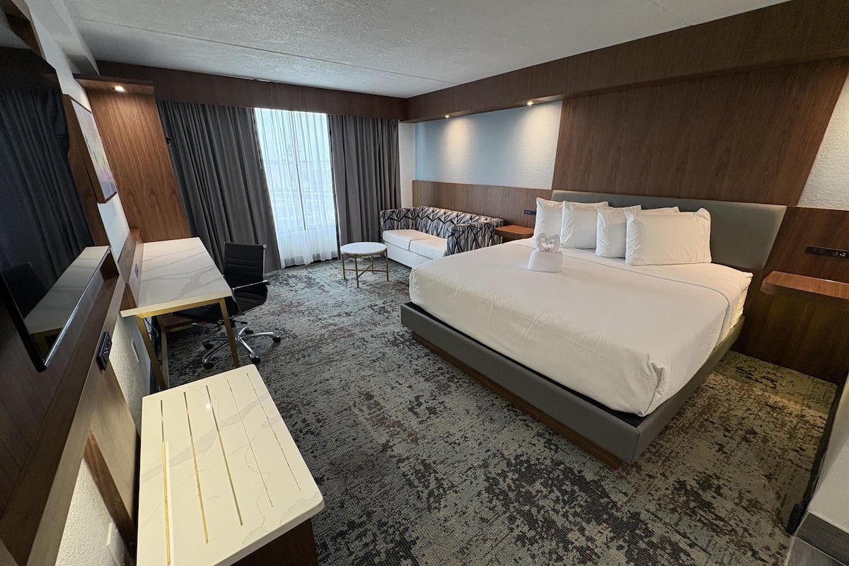 A hotel room with a large bed, a desk with a chair, a sofa, and a TV.