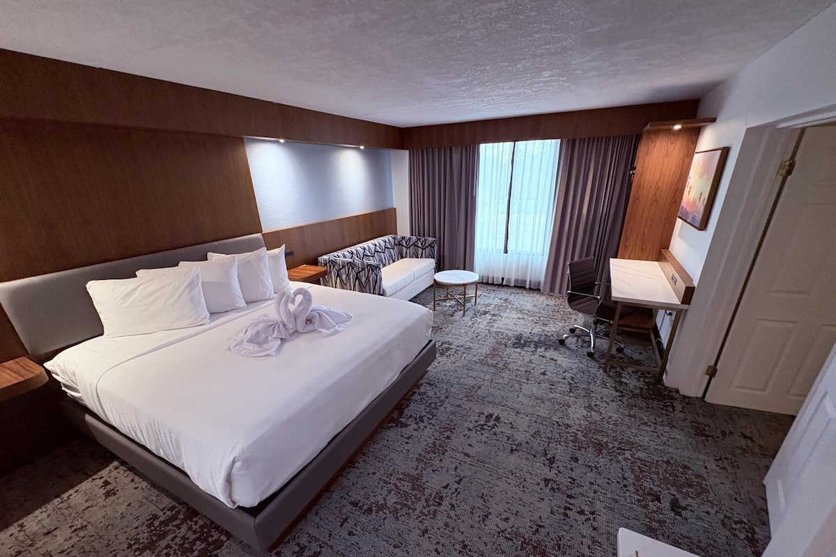 A hotel room with a large bed, a desk, a chair, and a small table.