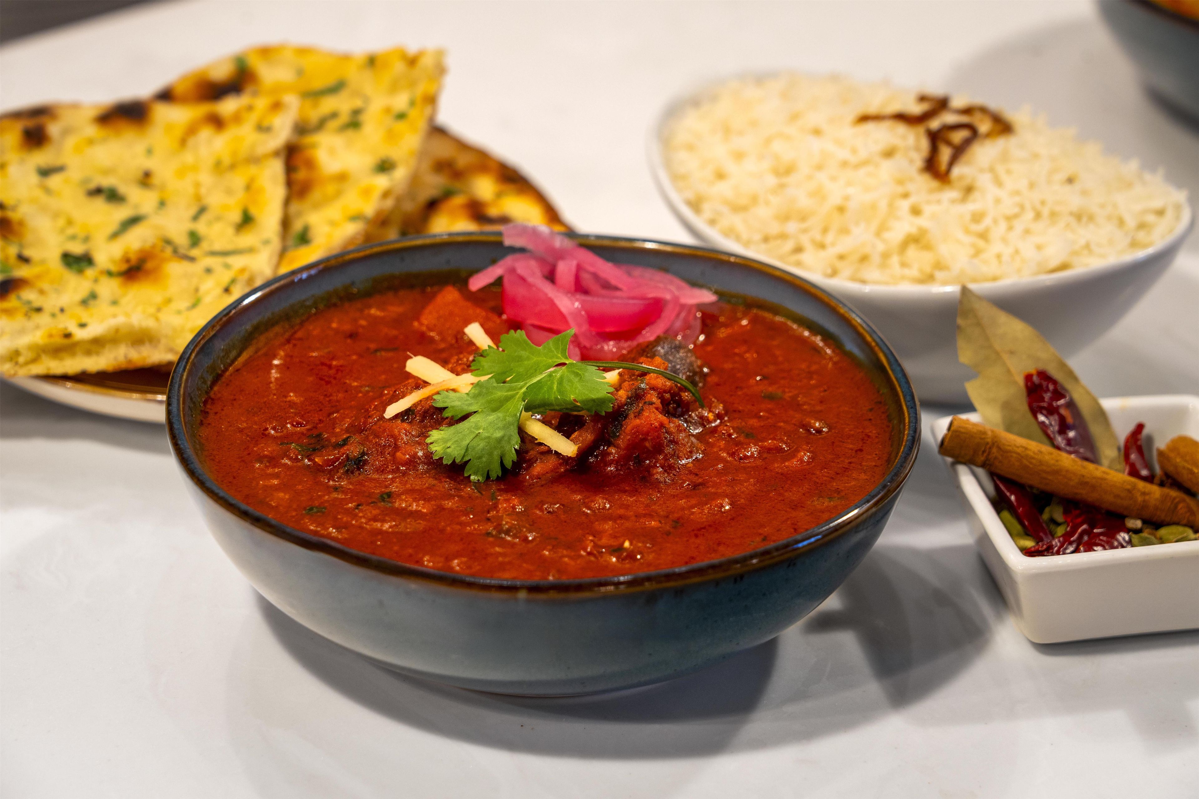 A bowl of curry with a garnish, accompanied by flatbread and rice.