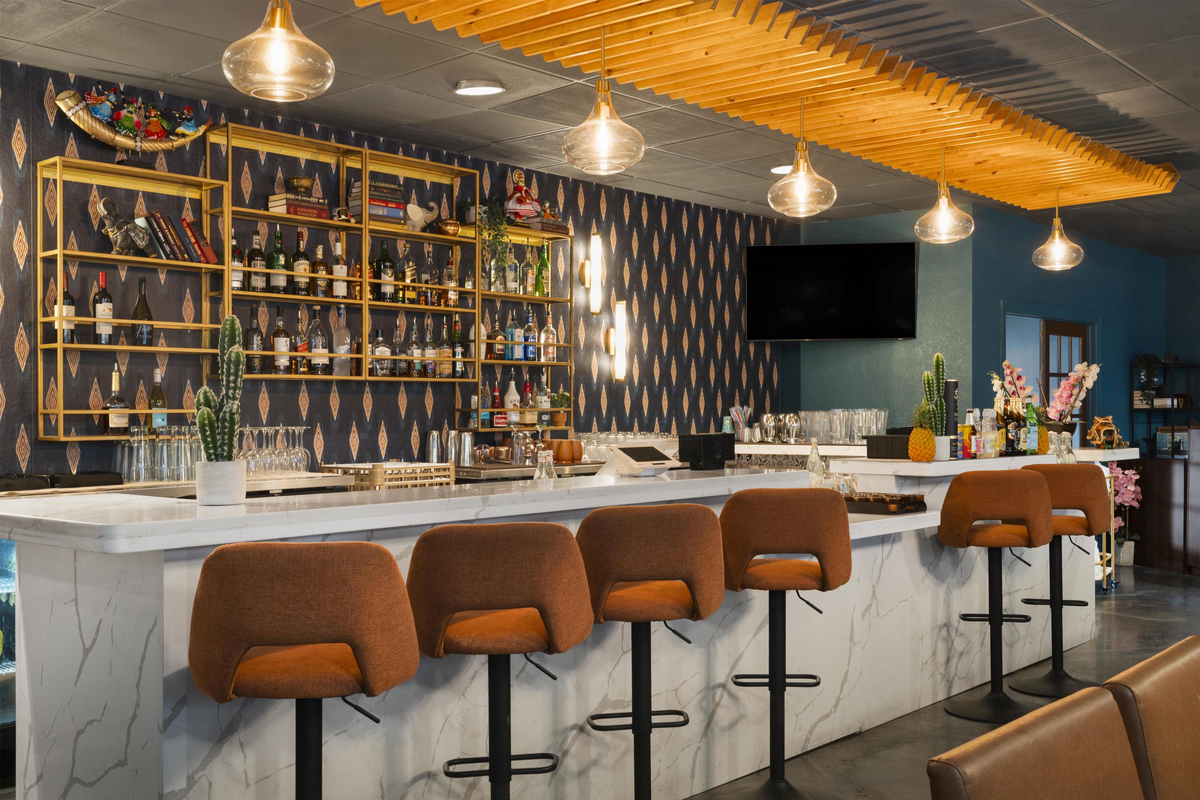 A bar area with a marble countertop, multiple stools, and a variety of bottles and glasses on shelves.