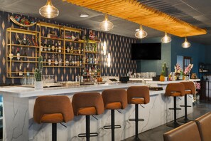 Una zona de bar con mostrador de mármol, varios taburetes y una variedad de botellas y copas en estanterías.