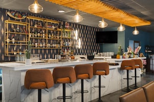 A bar area with a marble countertop, multiple stools, and a variety of bottles and glasses on shelves.