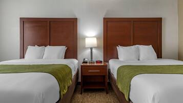 A hotel room with two single beds, a nightstand with a lamp, and a green throw blanket.
