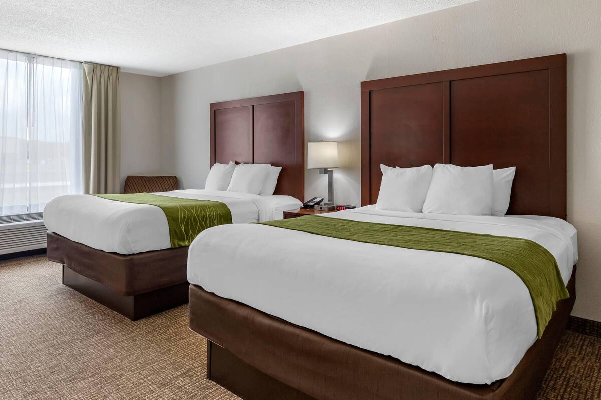 A hotel room with two beds, a desk, a chair, a lamp, and a window with curtains.