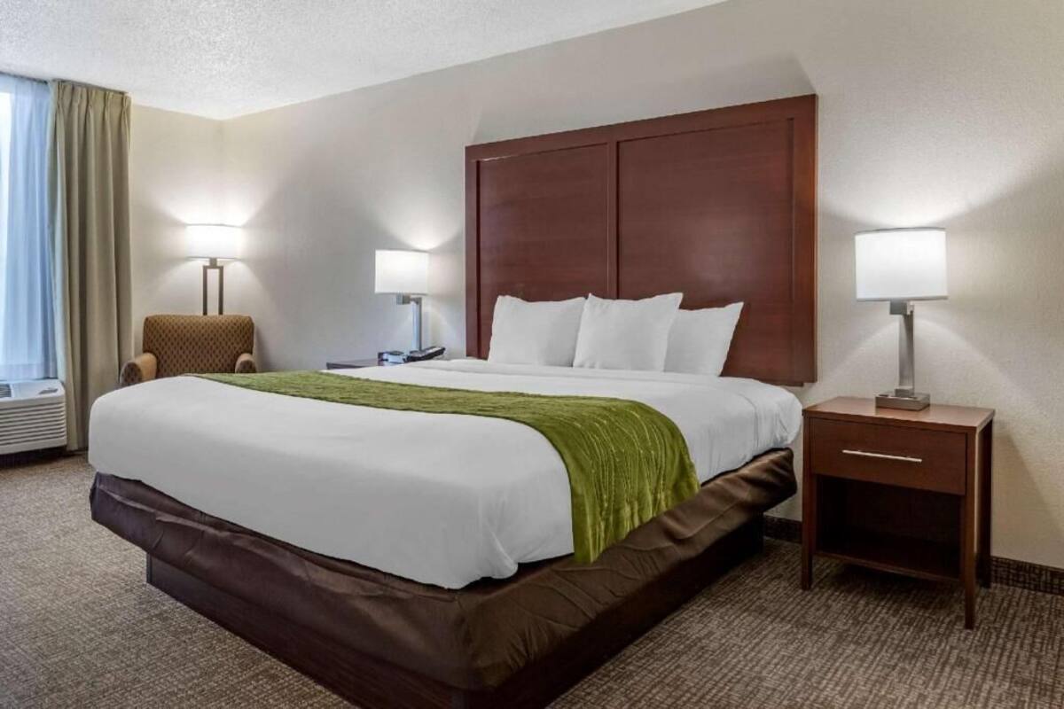 A hotel room with a large bed, two bedside lamps, a small table, and a chair.
