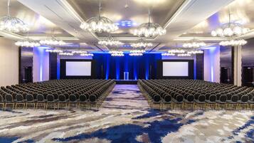A conference room with rows of chairs, a large screen, and a stage with blue lighting.