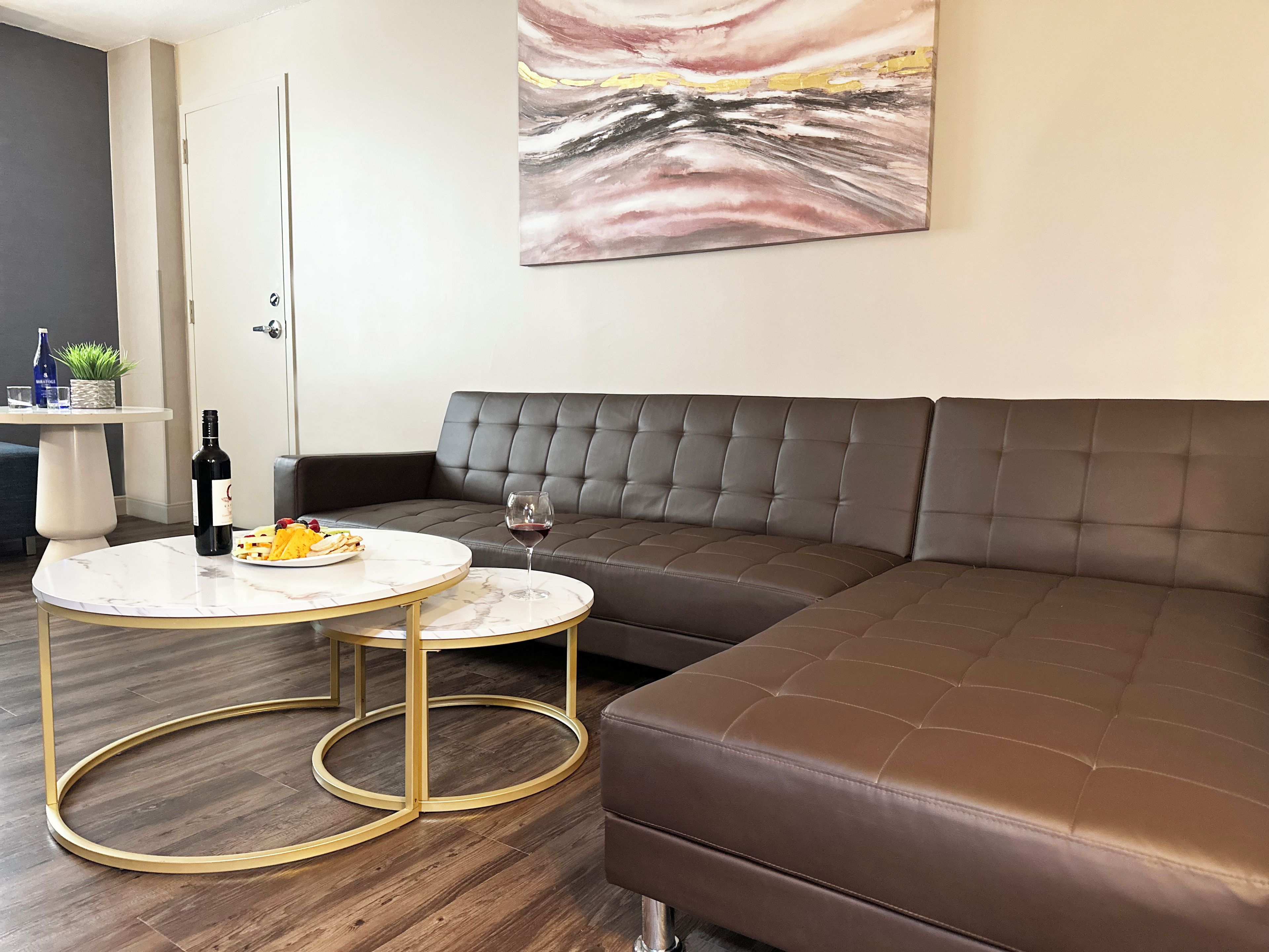 Een moderne woonkamer met een bruine leren bank, een marmeren salontafel met gouden poten, en een wijnglas.