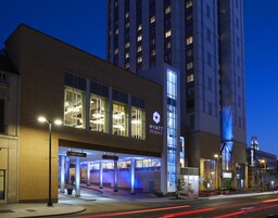 Una entrada de hotel moderna con un letrero visible que indica “SÓLO SALIDA”, el logotipo de “HYATT” y una fachada bien iluminada.