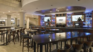 A modern bar area with multiple seating options, a television screen, and a variety of liquor bottles. - Hyatt Regency Rochester (Rochester)