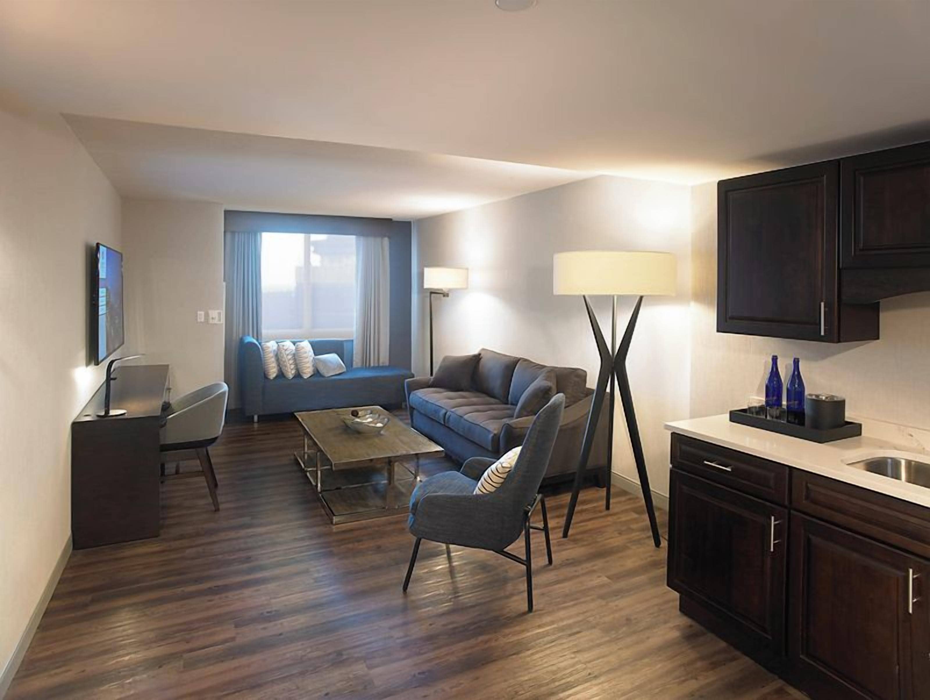 A compact living space with a sofa, armchairs, a coffee table, a TV, and a kitchenette.