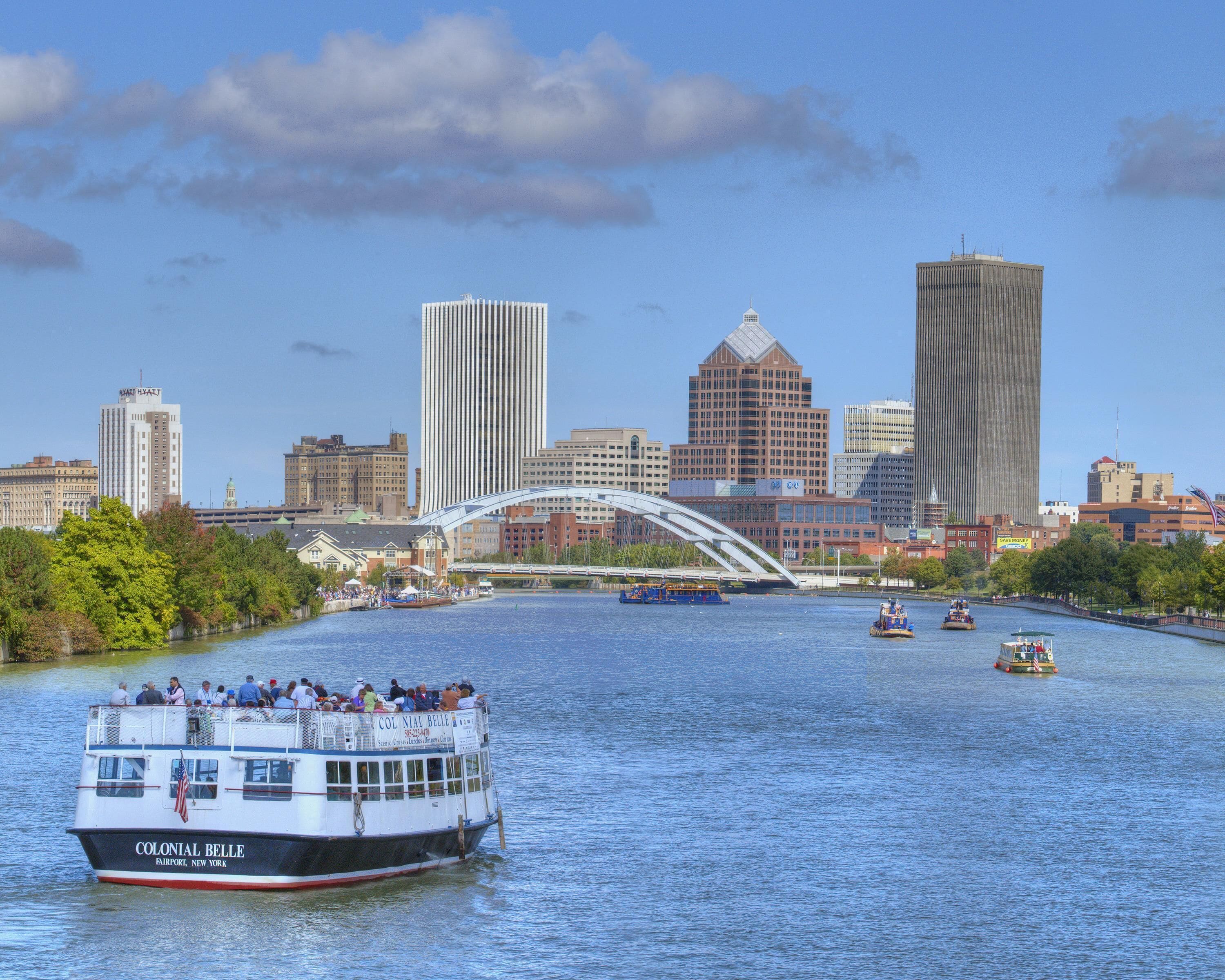 A river with a boat named 'Colonial Belle' and a city skyline in the background.