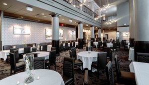A multi-level dining area with round tables, black chairs, and a patterned carpet.