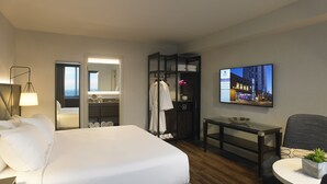A hotel room with a bed, a desk, a chair, a TV, a wardrobe, and a bathroom with a mirror and sink. - Hyatt Regency Rochester (Rochester)