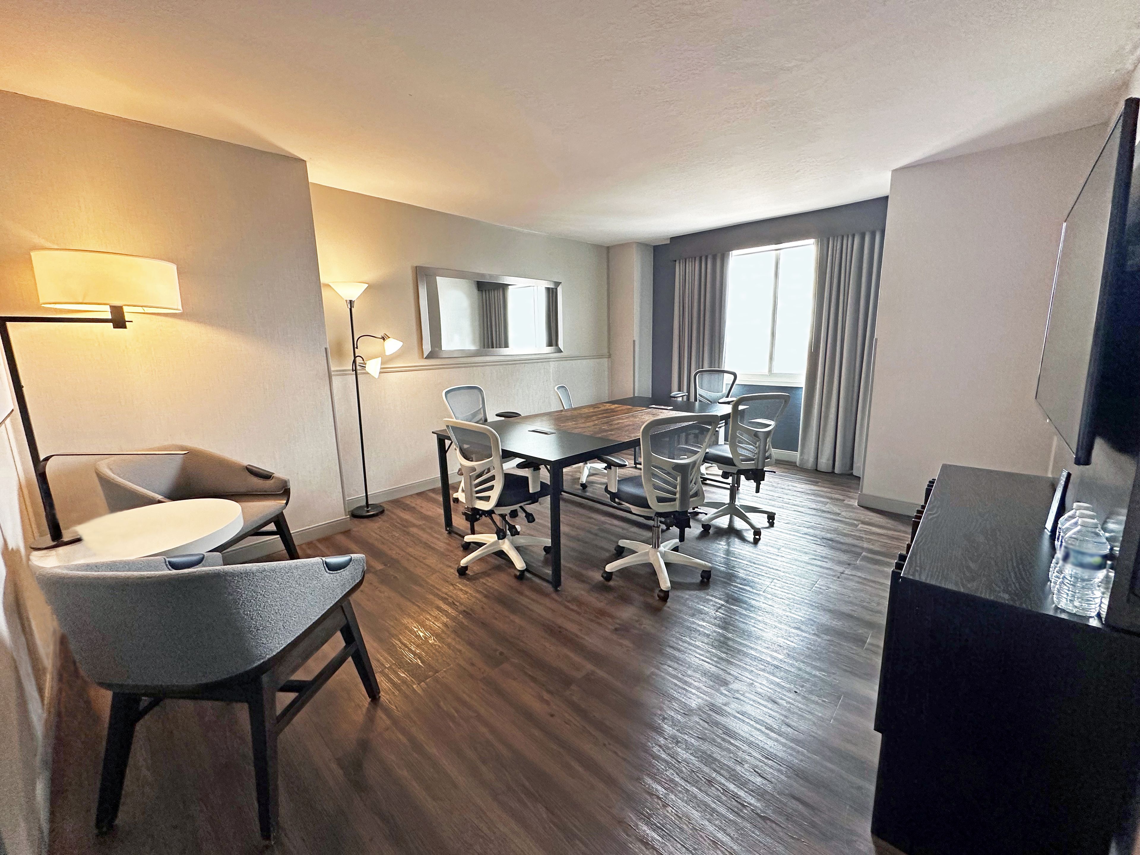 Un salón de conferencias de hotel con una larga mesa, varias sillas, un televisor y una lámpara de pie.