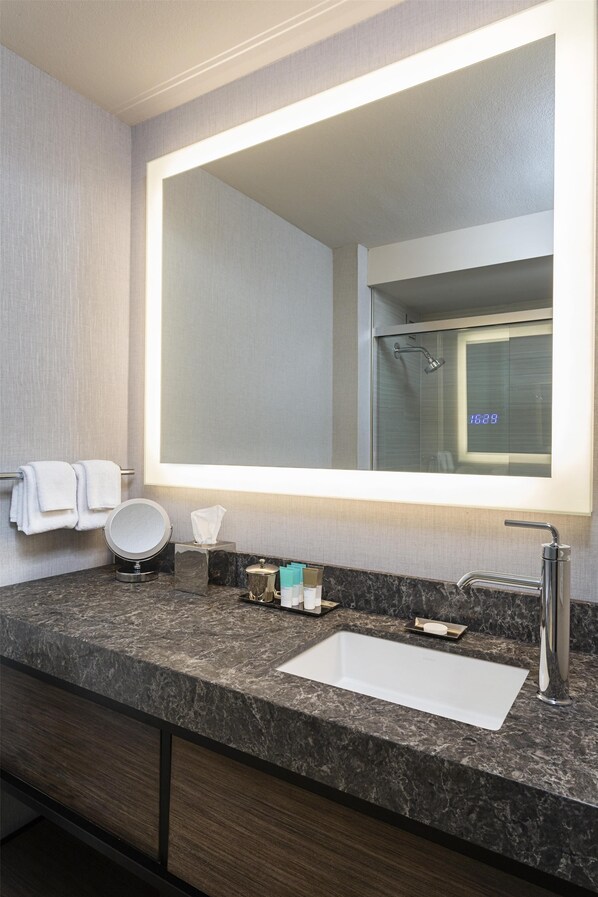 A bathroom with a large mirror, a sink, a towel rack, and a shower visible in the reflection.