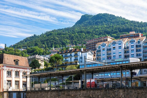 A train station with a covered platform, a building with a sign 'La Reine', and a mountainous backdrop.
