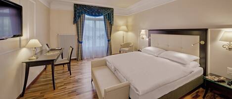 A hotel room with a bed, bedside tables, a desk, a chair, and a television.