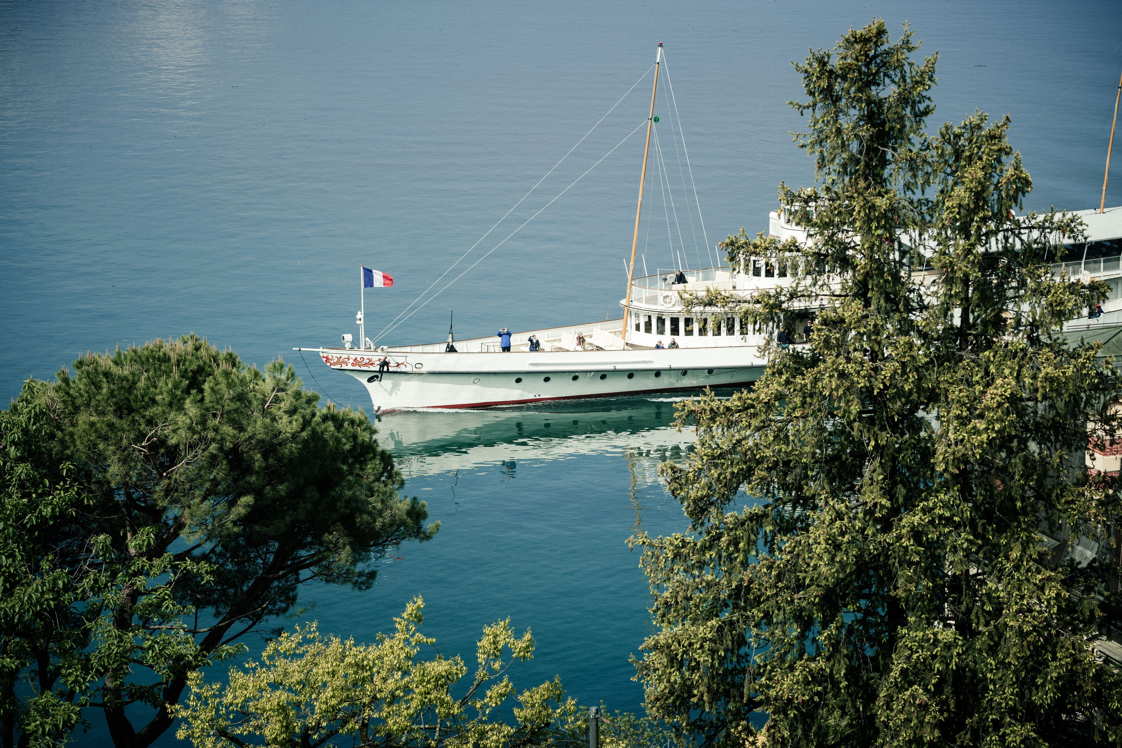 A boat docked at a marina with a flag, surrounded by trees.