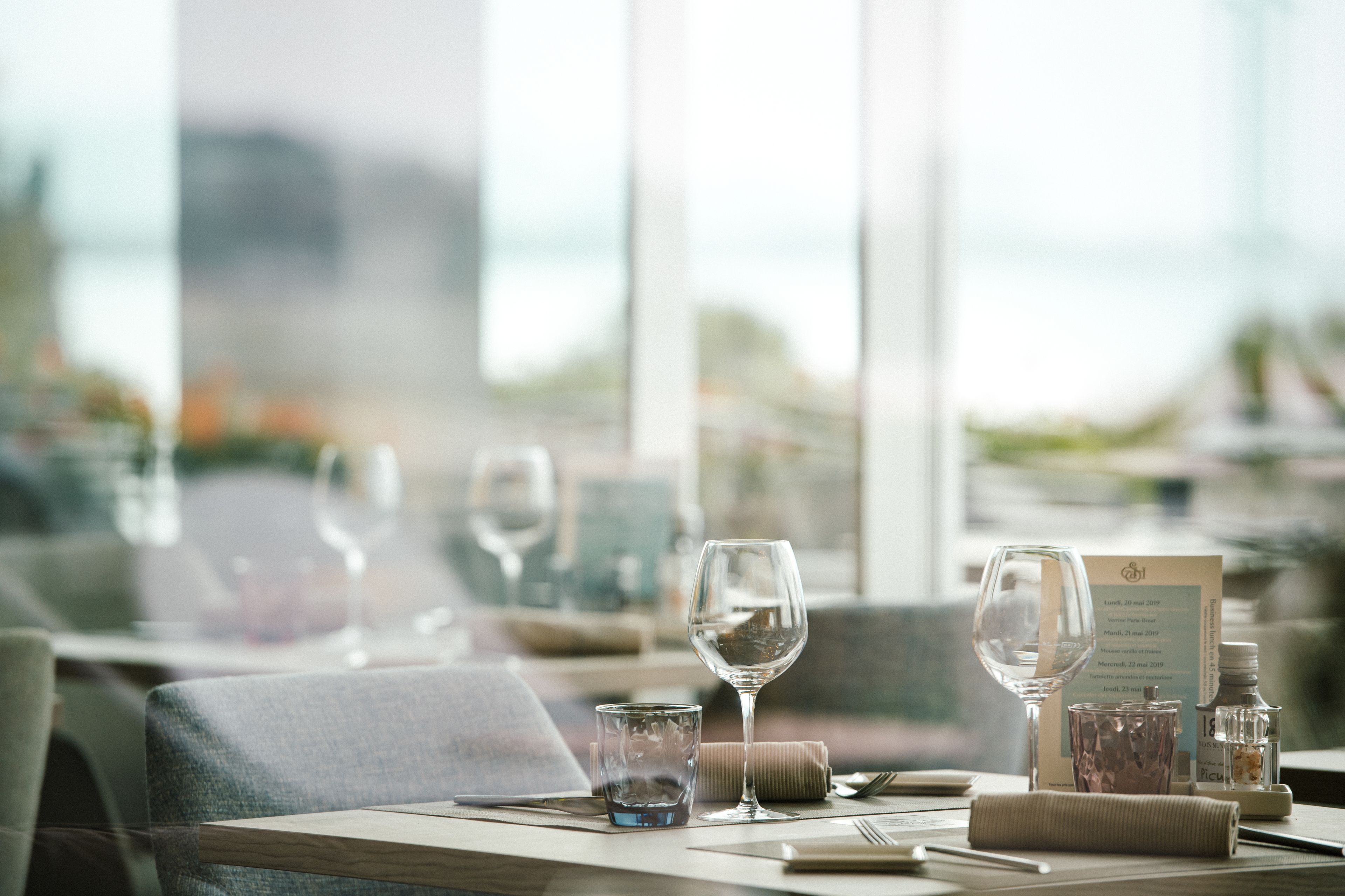 Une table à manger dressée avec des verres à vin, un menu et une bouteille d’eau.