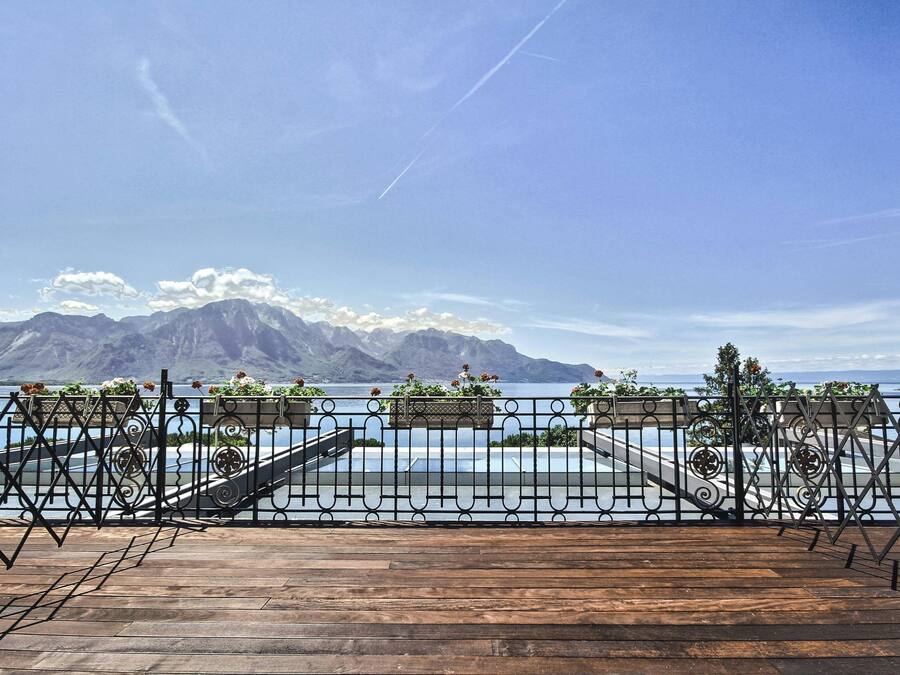 A wooden deck with a metal railing overlooking a body of water and mountains.