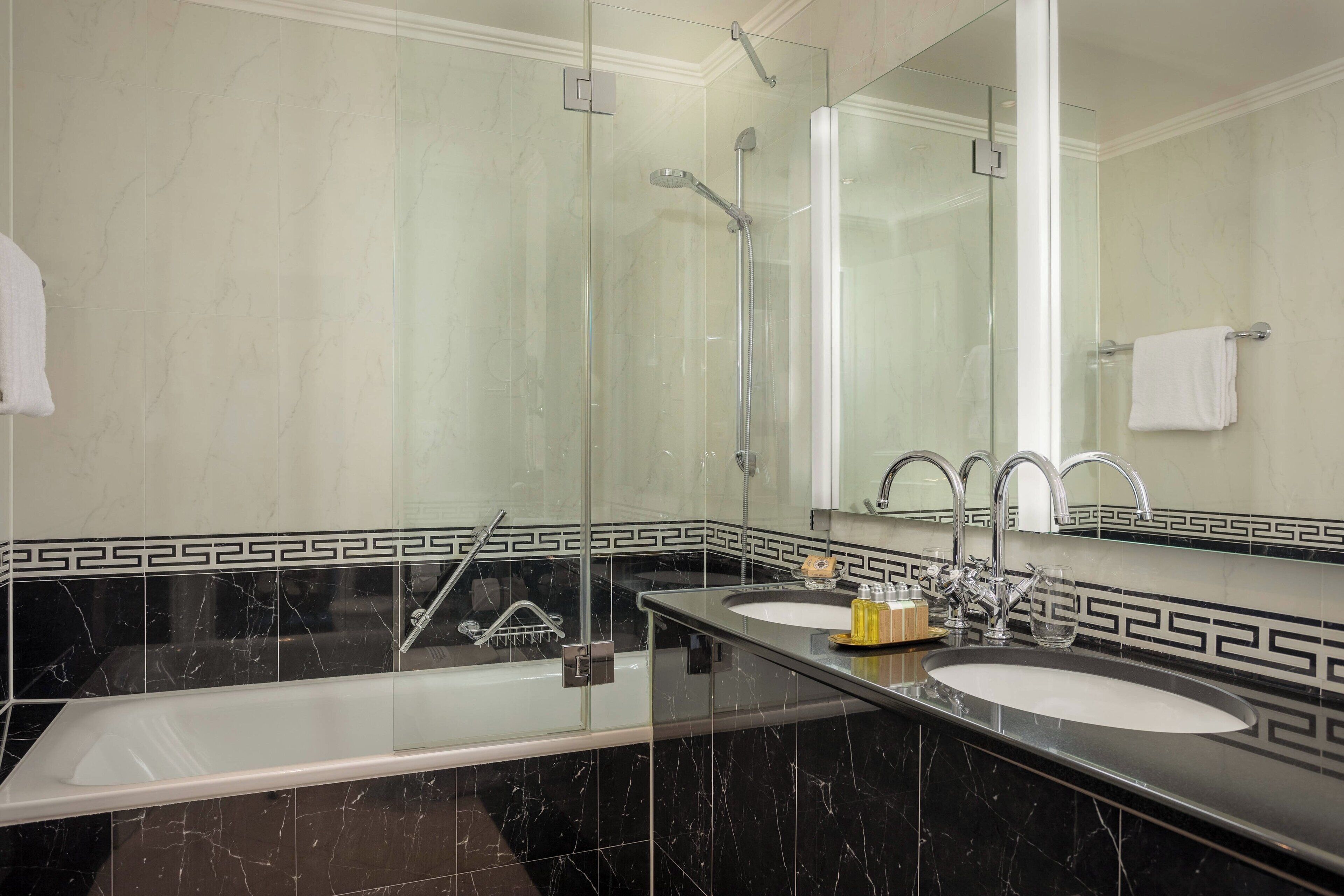 A modern bathroom with a large mirror, two sinks, a shower, and a bathtub.
