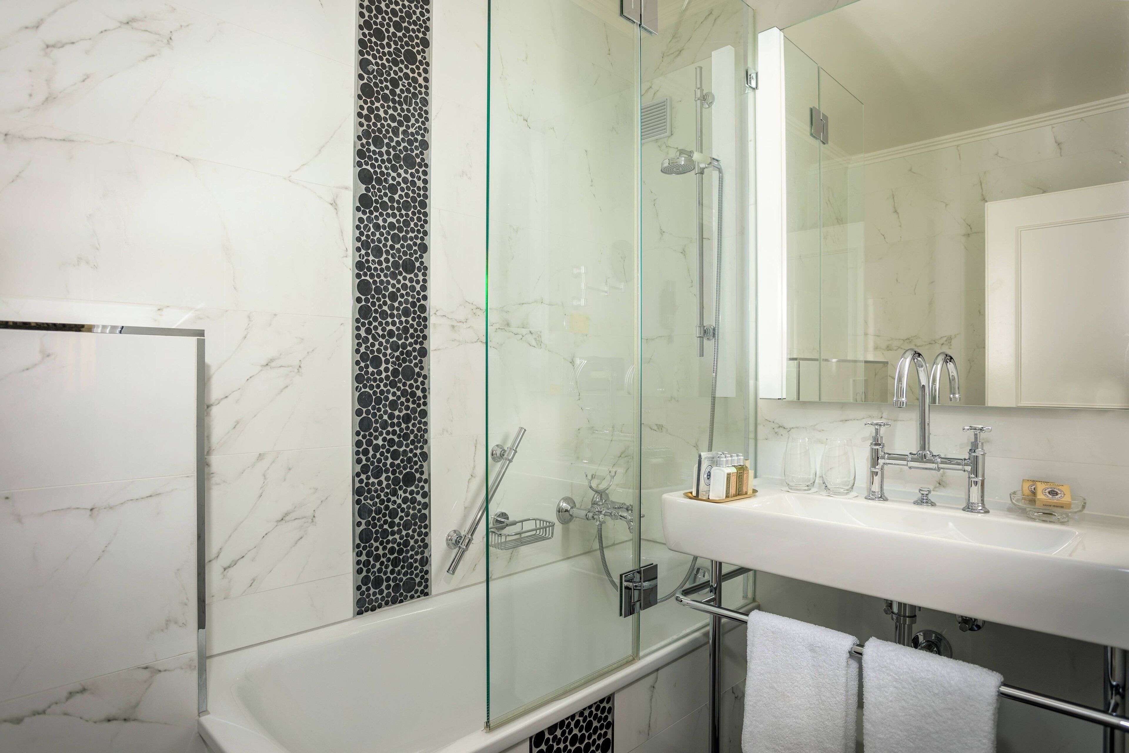 Un bagno moderno con doccia vetrata, un lavandino bianco con specchio e una parete rivestita in marmo.