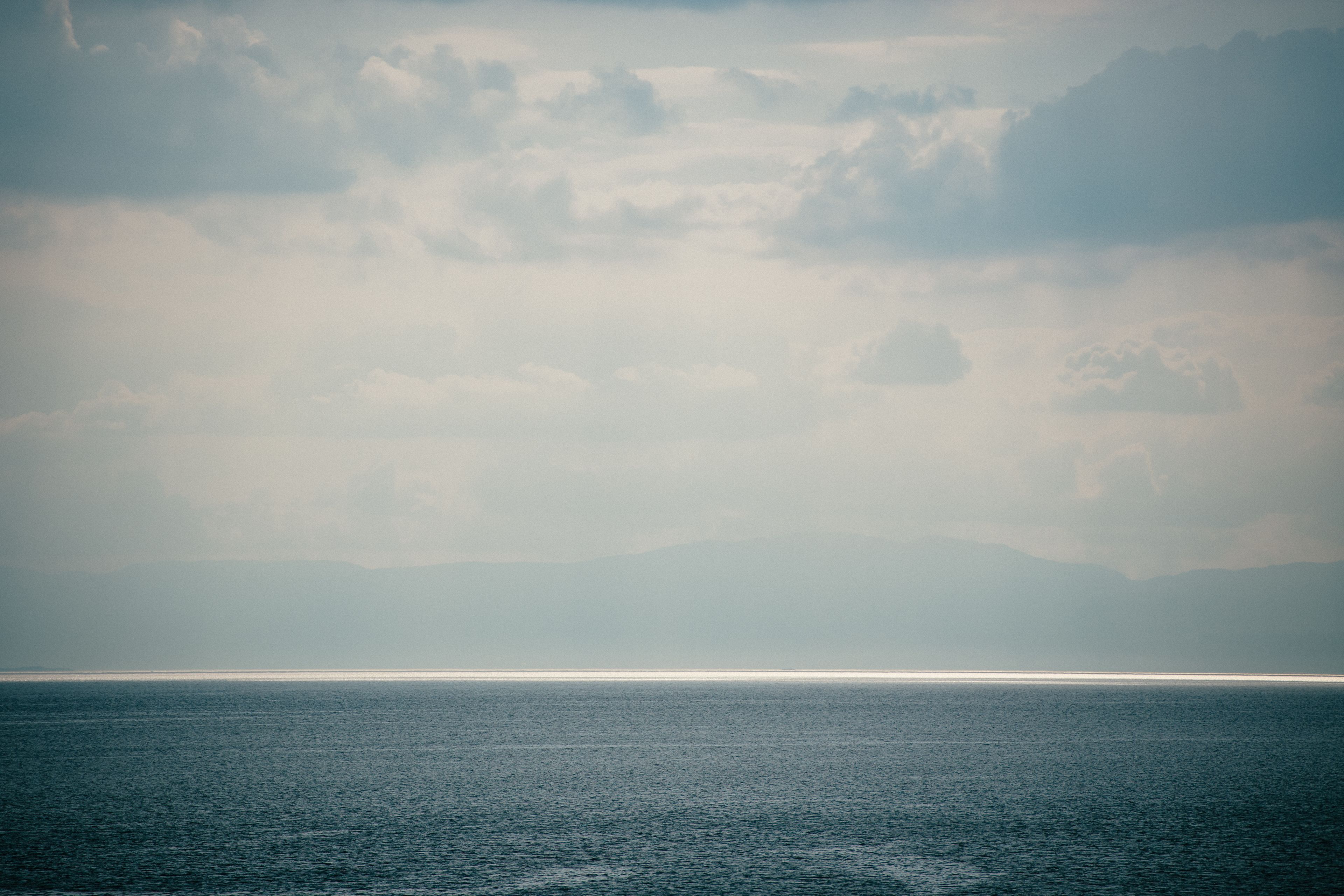 Mare tranquillo con una catena montuosa in lontananza sotto un cielo nuvoloso.