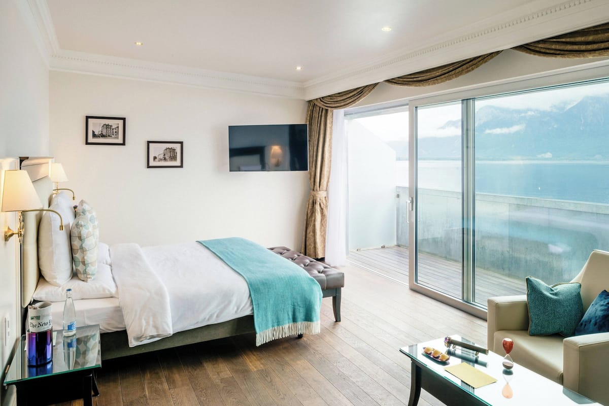 Una habitación de hotel con cama, sofá, televisión y un ventanal con vistas al mar.