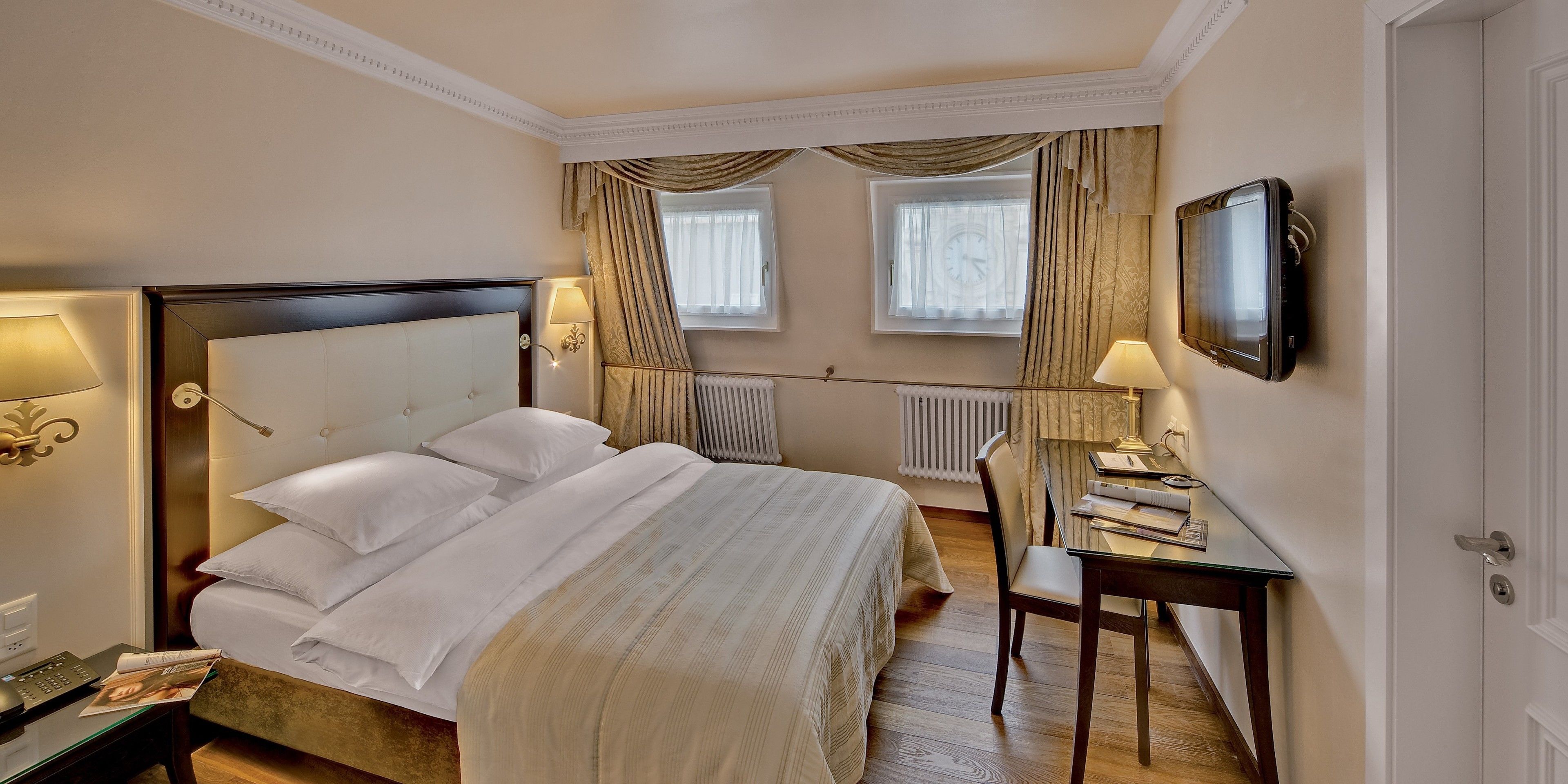 Une chambre d’hôtel avec un grand lit, un bureau avec une chaise, une télévision et une fenêtre avec des rideaux.