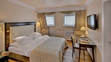Une chambre d’hôtel avec un grand lit, un bureau avec une chaise, une télévision et une fenêtre avec des rideaux.