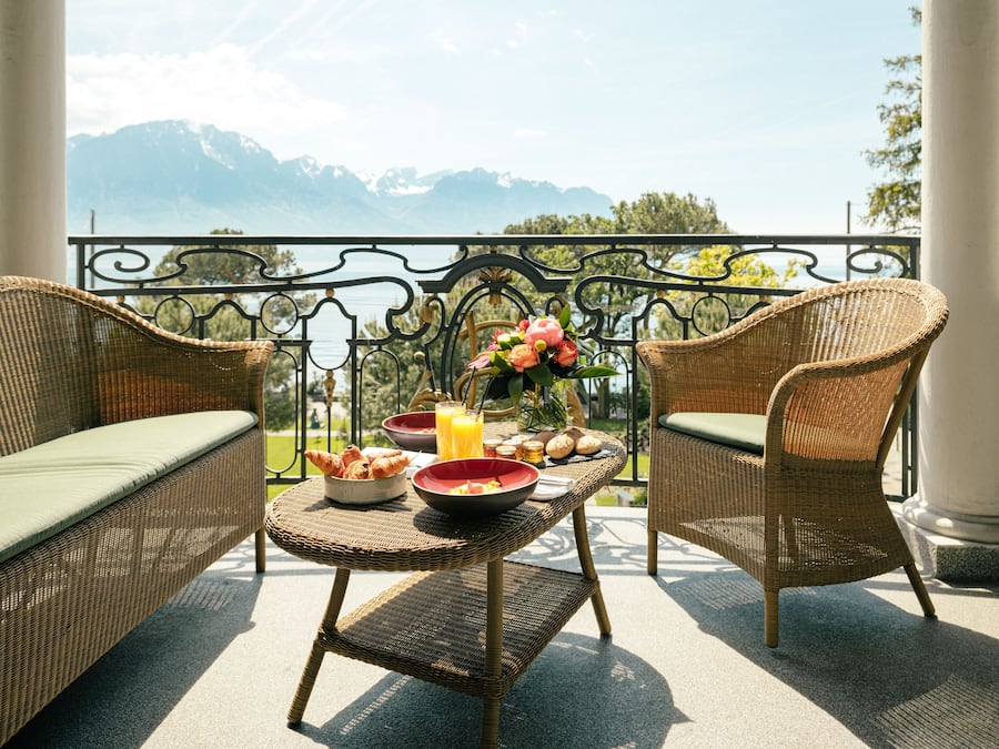 Un balcón con mobiliario de mimbre, una mesa con alimentos para el desayuno y vistas a las montañas.