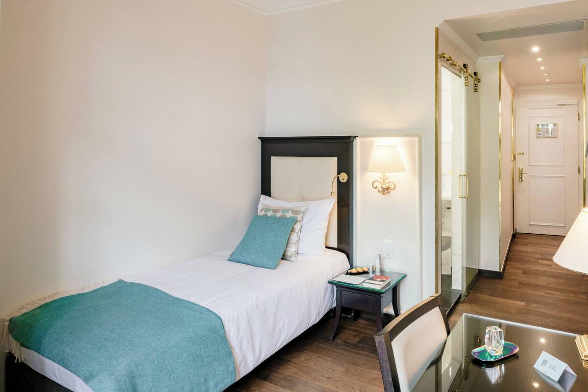 Una habitación de hotel con cama, mesita de noche, lámpara y espejo.