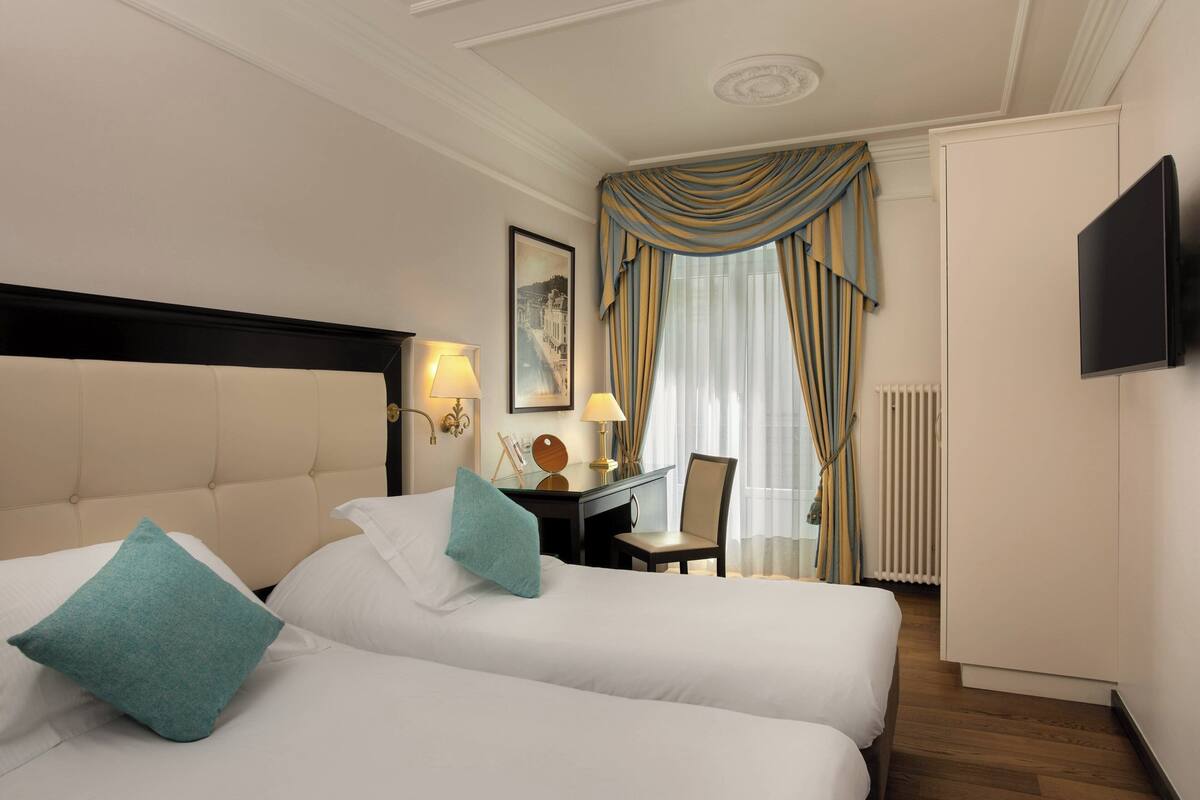 Habitación de hotel con dos camas, un escritorio, una silla, un televisor y una ventana con cortinas.