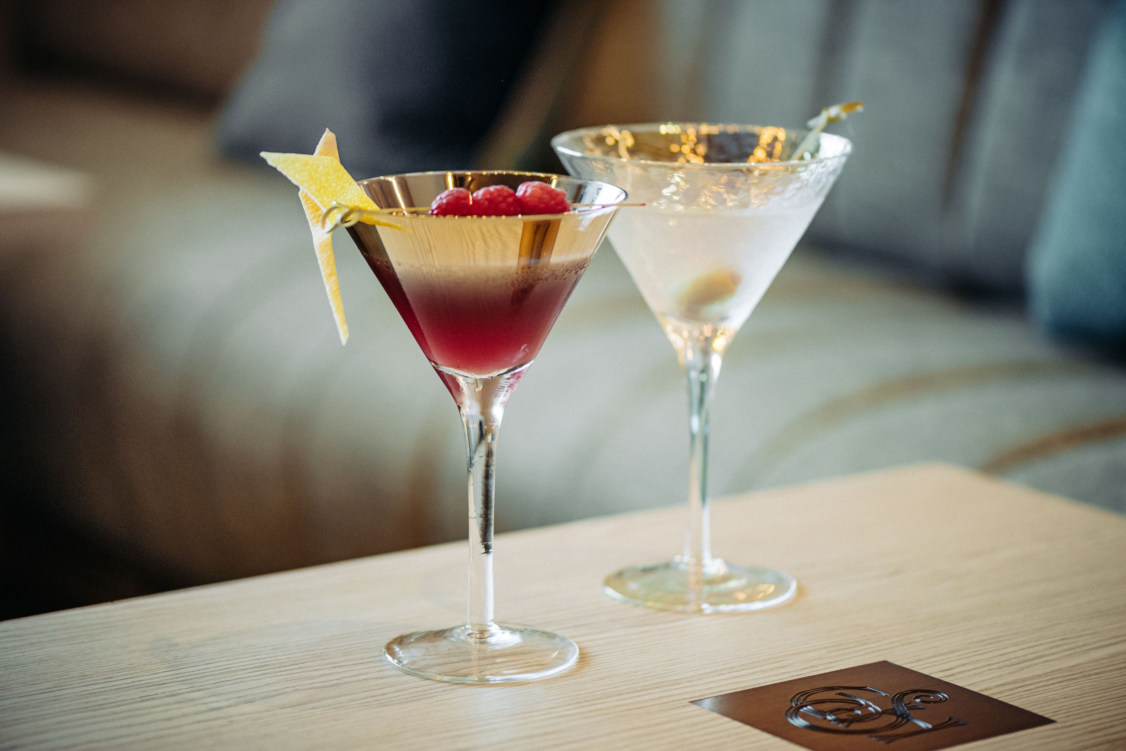 Two martini glasses on a wooden table with a blurred background.