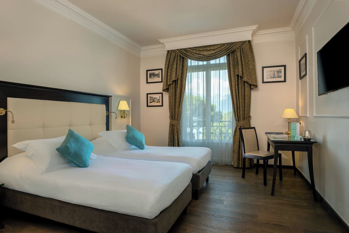 Una habitación de hotel con una cama grande, dos mesitas de noche, un escritorio con una silla y un televisor en la pared.